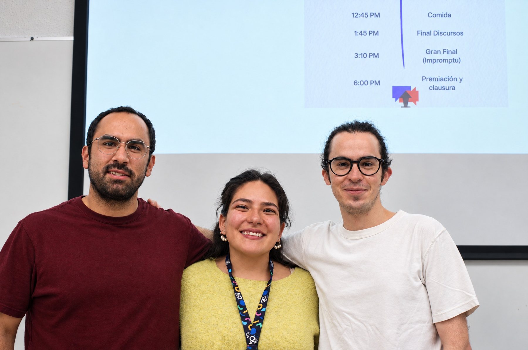 Tres integrantes del equipo frente a la pantalla con el programa del torneo